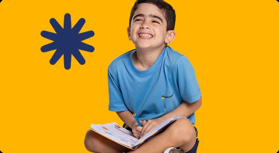 Aluno do Contemporâneo sorrindo, com caderno no colo, em frente a fundo amarelo com grafismo de asterisco